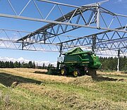 Mähdrescher arbeitet unter aufgeständerter PV-Anlage