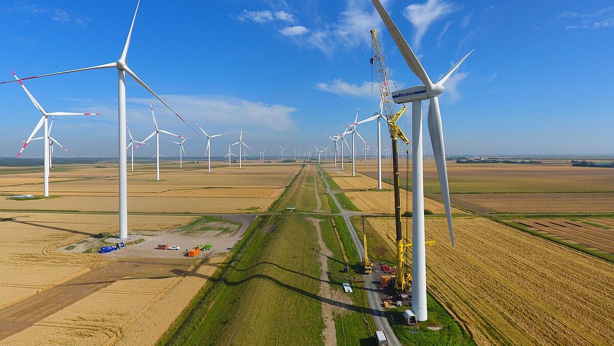 Blick in einen Windpark, an einer Anlage im Vordergrund sind Kranarbeiten zu erkennen