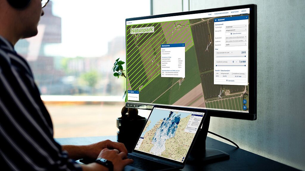 A man sits in front of a screen showing different aerial photos and maps
