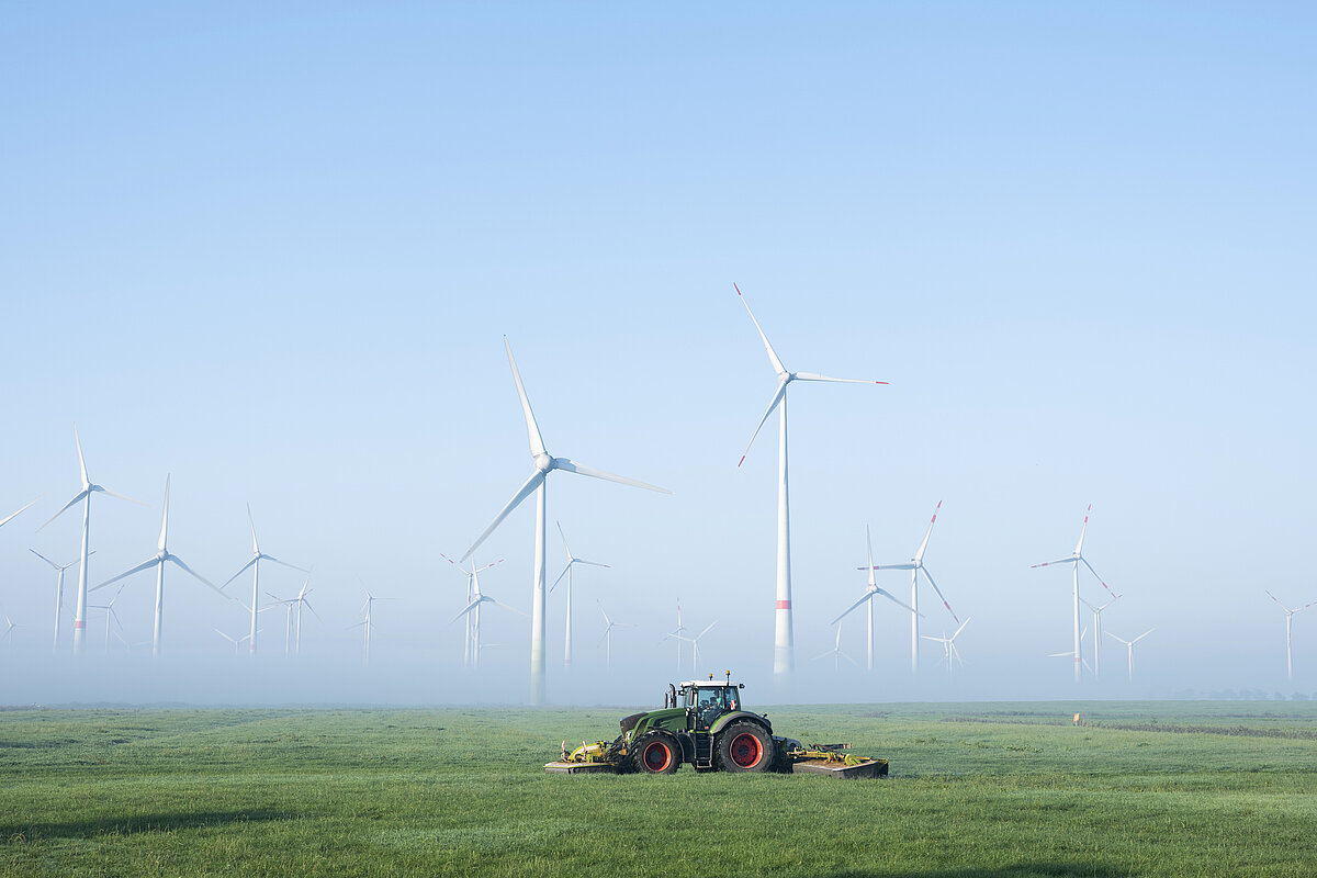 Ein Traktor mäht eine Weide vor einem Windpark.