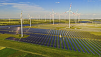 A solar park is being built within an existing wind farm. Visible are wind turbines, completed sections of the solar park, and module mounting frames before the panels are installed.