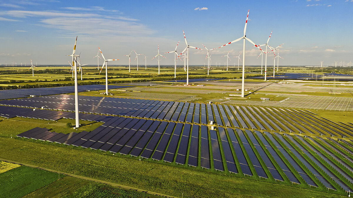 A solar park is being built within an existing wind farm. Visible are wind turbines, completed sections of the solar park, and module mounting frames before the panels are installed.